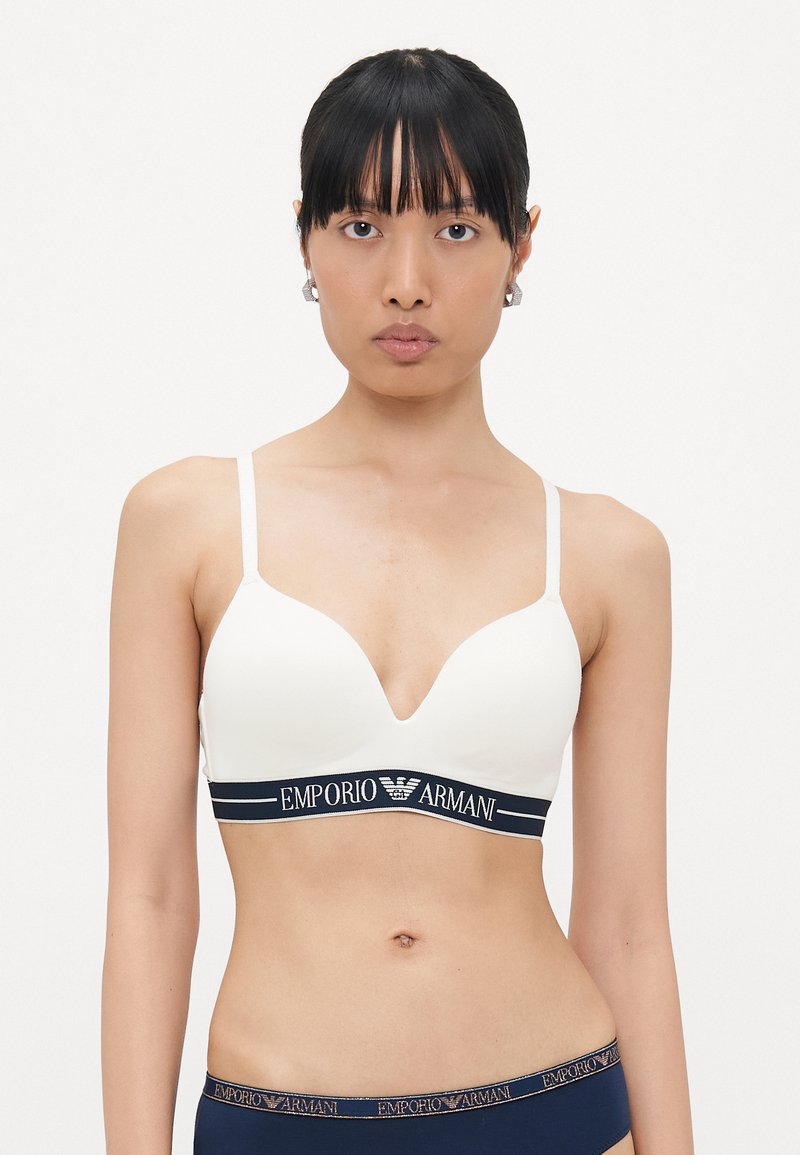 White plunge bra with adjustable straps, featuring a navy elastic band with "EMPORIO ARMANI" logo. Smooth texture, minimalist design.