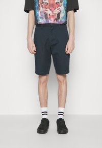 Shorts navy fabriqués en tissu résistant, avec une coupe classique. Associés à des baskets noires et des chaussettes blanches à rayures noires. T-shirt avec un graphique de tigre au-dessus.