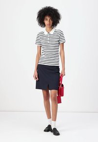 Rutet poloshirt i hvit og marineblå, sammen med et marineblå skjørt med sliss foran. Tilbehør inkluderer en rød håndveske. Svarte sko og hvite sokker.