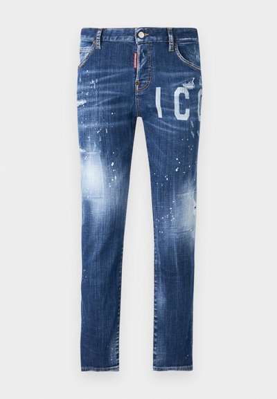 Sügavsinised teksased, millel on kulumise detailid, pritsimisefektid ja suured valged kirjad. Omab klassikalist viie taskuga disaini.