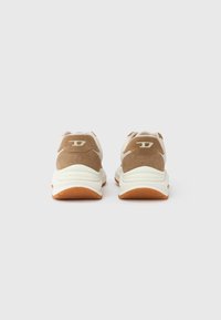 Καφέ και λευκά αθλητικά παπούτσια με υφή σουέτ στο επάνω μέρος, επενδεδυμένο κολάρο και λαστιχένια σόλα. Διαθέτουν διακριτικό λογότυπο στη φτέρνα.