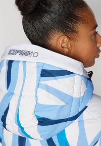 Blau-weiße gesteppten Jacke mit hohem Kragen, ausgeführt mit einem schwarzen Logo am Kragen und einer gesteppten Textur.