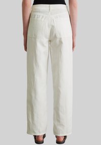 Białe spodnie o szerokich nogawkach i wysokim stanie. Posiadają dwie tylne kieszenie oraz gładki, teksturowany materiał. Noszone z czarnymi butami.