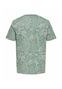 Camiseta verde claro de algodón suave, con un patrón floral blanco, cuello redondo y mangas cortas. La vista trasera resalta los detalles del diseño.