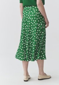 Jupe verte à pois avec un design fluide et un ourlet. Présente une texture légère et lisse ainsi qu'une fente sur le côté pour un mouvement facilité.
