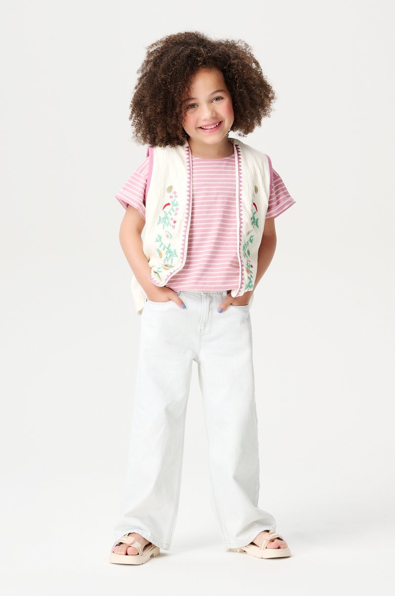 Gestreept roze shirt met korte mouwen, witte geborduurde gilet, lichtgewassen wijde spijkerbroek, en beige sandalen met een stevige zool.
