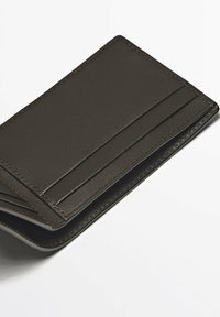 Portefeuille en cuir brun avec plusieurs emplacements pour cartes, une surface texturée et des coutures contrastantes le long des bords. Design rectangulaire compact.