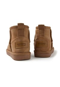 Botines de ante marrón con un acabado texturizado, que cuentan con un panel lateral de tela, suela plana y una etiqueta de marca en la parte trasera.