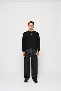 Black textured long-sleeve shirt, high-waisted dark denim jeans, paired with glossy black shoes and a gold pendant necklace.