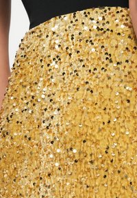 Ingrandimento di una gonna coperta di paillettes dorate indossata con un top nero, che mette in evidenza il tessuto lucido e testurizzato e le paillettes riflettenti.
