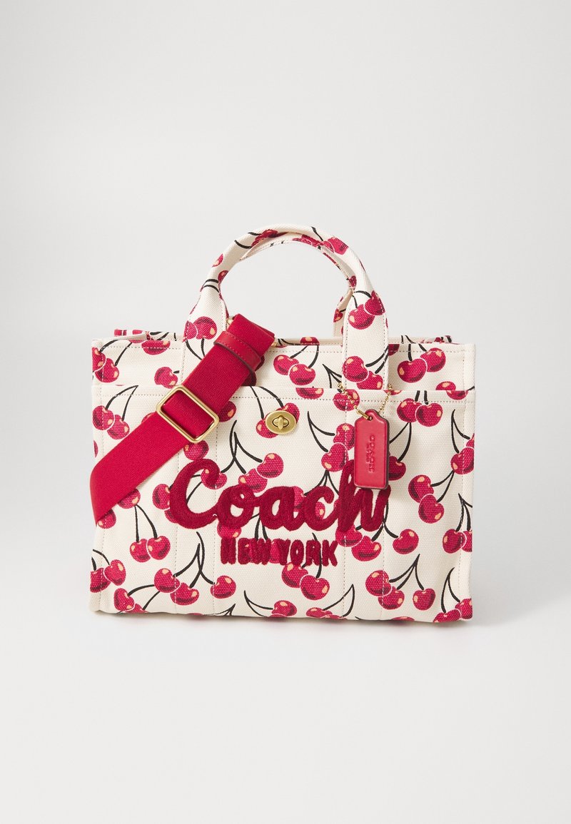 Petit sac à main blanc avec imprimé cerises rouges, bandoulière rouge réglable et logo brodé "Coach New York" rouge à l'avant.