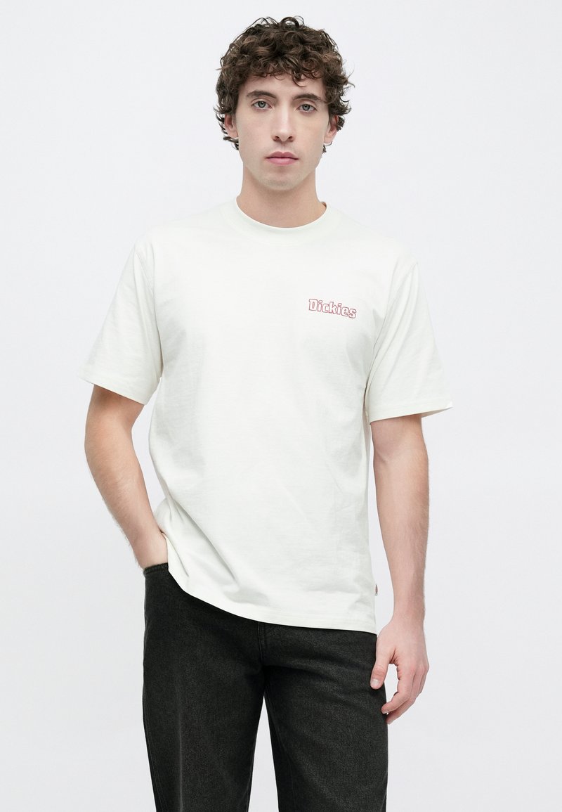 Cremefarvet t-shirt med korte ærmer i bomuld, med et lille rødt "Dickies"-logo på brystet og en afslappet pasform. Kombineret med mørke jeans.