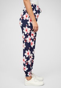 Pantaloni navy con grandi motivi floreali bianchi e rosa, con vita elastica e polsini. Abbinati a sneakers bianche.