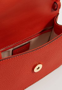 Czerwona torebka ze skóry o fakturze, z złotym zatrzaskiem i kremowym wnętrzem. W środku znajduje się metka marki oraz dwie kieszenie do organizacji.