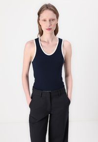 Navy ribbed tank top with white trim, featuring a scoop neckline. Paired with black tailored trousers, both have a fitted silhouette.
