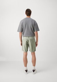 Maglietta grigia a maniche corte, tessuto morbido; pantaloni corti verde chiaro, con risvolti, due tasche posteriori, patch logo discreto. Vestibilità casual, design semplice.