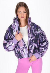 Polstret jakke i lilla og sort marmor mønster med aftagelig hætte og ribbetræk ved håndleddene. Båret åben over en hvid top og pink leggings.