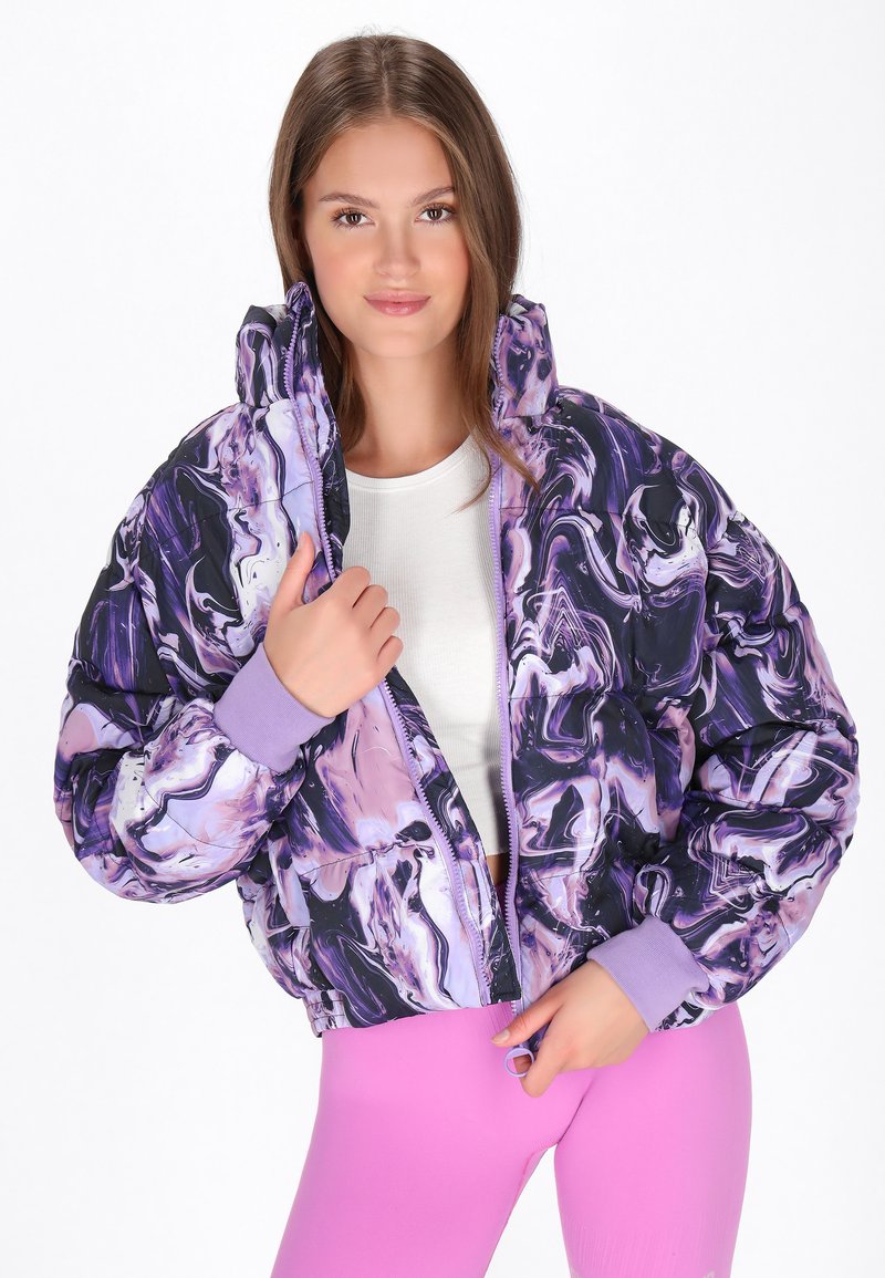 Polstret jakke i lilla og sort marmor mønster med aftagelig hætte og ribbetræk ved håndleddene. Båret åben over en hvid top og pink leggings.