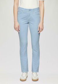 Heled sinine, täpselt istuv denim teksapüksid klassikalise viie taskuga disainiga ja nupuga kinnitusega, koos valgete tossudega. Sile tekstuur ja sirged sääred.