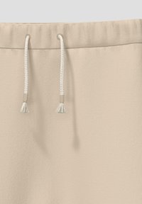 Beige sweatpants met een zachte textuur, een elastische tailleband en koorden met kwastjes. Minimalistisch ontwerp, zonder patronen.