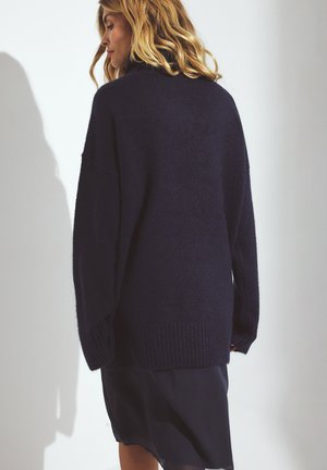 Przesadzony niebieski sweter o miękkiej fakturze, z prążkowanymi mankietami i dołem. Luźny krój, opadające ramiona i minimalne detale z tyłu.