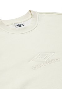 Felpa a girocollo beige chiaro realizzata in tessuto morbido, con un logo "Umbro" ricamato in rilievo di colore bianco e un design geometrico sul davanti.