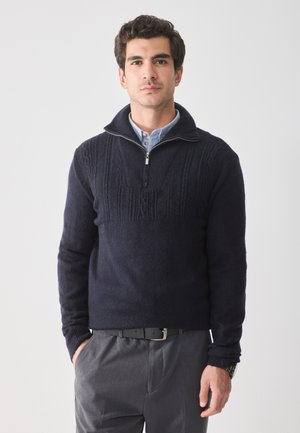 Navy Quarter-Zip Pullover-Sweater mit strukturiertem Strickmuster auf der Vorderseite, aus weichem Material; über einem hellblauen Hemd mit Kragen getragen.