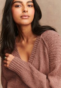 Gestrickter Pullover in staubrosa, mit V-Ausschnitt, gerippten Bündchen und strukturierten Mustern. Weiches, lässiges Design mit leichter Sprenkelung.