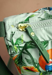 Borsa in tessuto con motivo floreale verde e arancione, con una cerniera dorata, dotata di un tirante verde con la scritta "Cath Kidston" in rilievo. Texture morbida.