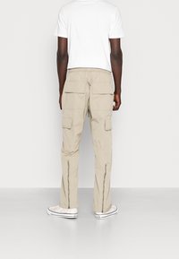 Béžové cargo kalhoty s několika bočními kapsami, elastickým pasem a zipovými manžetami. Kombinované s bílým tričkem s kulatým výstřihem a teniskami.