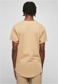 Tricou bej cu mânecă scurtă și margine curbată. Fabricat din bumbac moale, având o croială lejeră și manșete răsucite pentru un plus de confort.