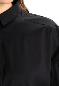 Camicia nera con colletto realizzata in tessuto morbido, caratterizzata da cuciture sottili e una vestibilità rilassata, con orlo diritto e senza decorazioni prominenti.