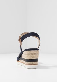 Námořnické plátěné klínové sandály s jutu tkanou patou, nastavitelným páskem kolem kotníku a hnědými koženými akcenty. Bílá gumová podrážka dodává kontrast.