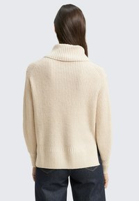 Beige gebreide trui met een schouderkraag, ribbelstructuur en een licht cropped ontwerp. Kenmerkt zich door een rechte zoom en verlaagde schouders.