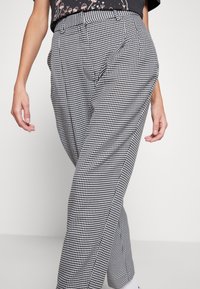 Black and white houndstooth patterned trousers with a loose fit, side pockets, and a high waist design. Soft fabric with subtle texture.