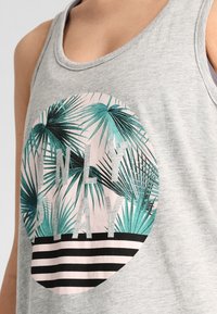 Canotta grigia chiara con un design circolare che presenta foglie di palma teal e nere, le parole "ONLY PLAY" e una parte inferiore a righe bianca e nera.