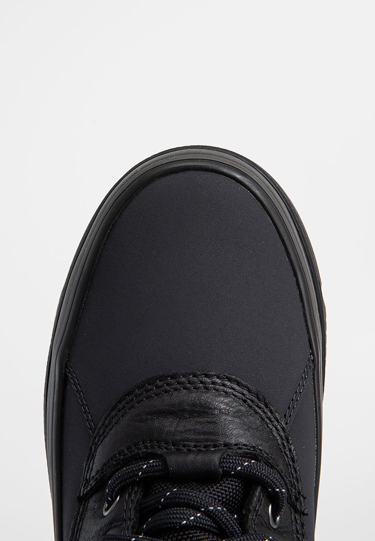 Nahaufnahme des vorderen Teils eines schwarzen Sneakers mit einer runden Zehenpartie, strukturierten Schnürsenkeln und genähten Lederdetails auf einem weißen Hintergrund.