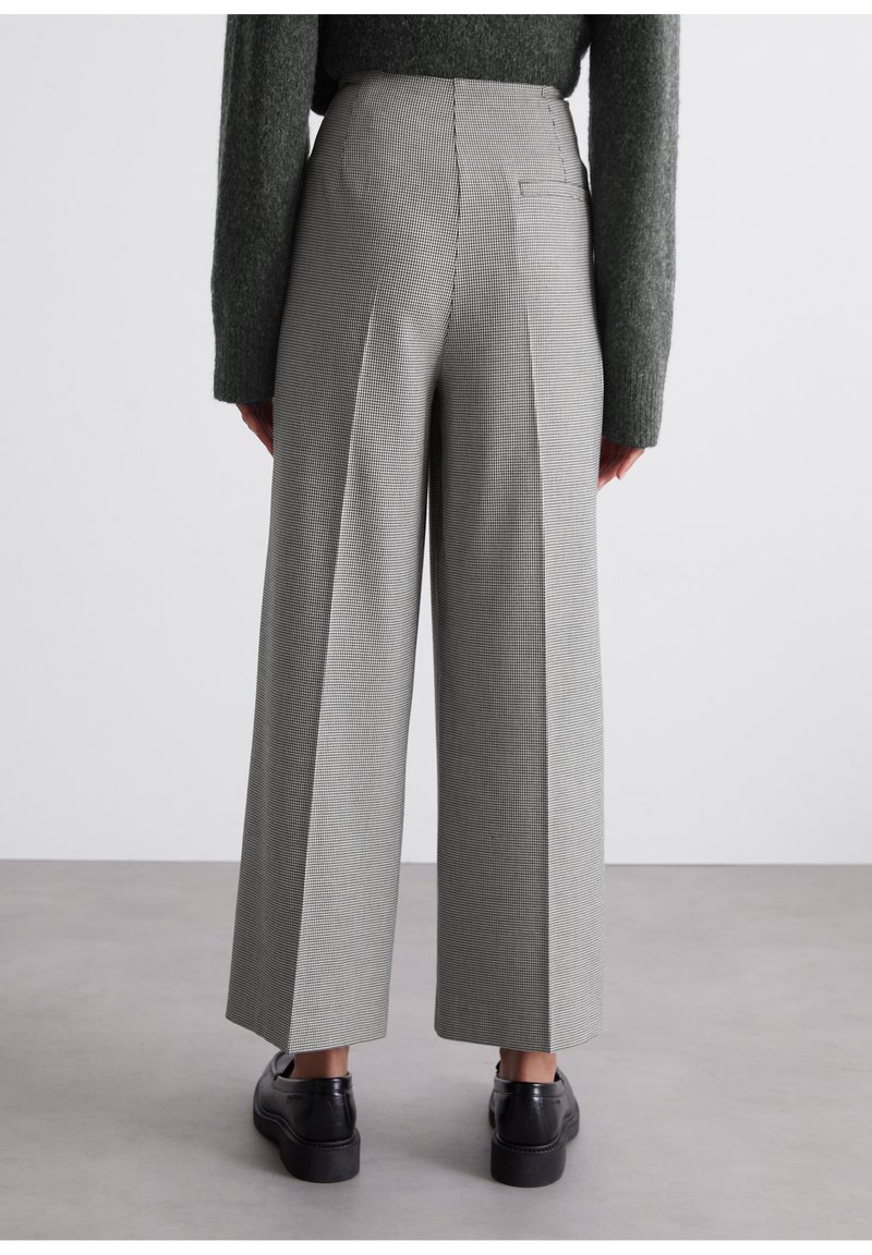 Grau karierte, taillierte Hose mit weitem Bein und mittelhohem Bund. Verfügt über eine Gesäßtasche und eine weiche Stofftextur. Getragen mit schwarzem Schuhwerk.