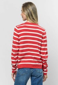 Červeno-biele pruhované sveter s dlhým rukávom, ktorý má rebrovaný golier a manžety, mäkký materiál a klasický strih. Nosený s modrými džínami.