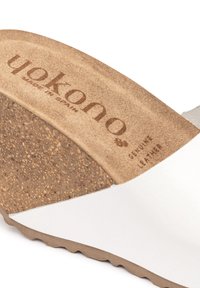 White leather slide sandal with a cork footbed, featuring a textured surface and printed branding on the insole. Rubber outsole for traction.