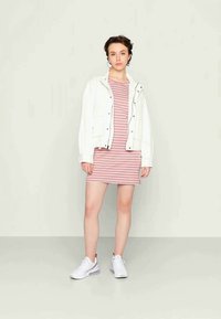 Casaco branco com fecho éclair sobre um vestido riscado em rosa e branco, complementado com sapatilhas brancas. Tecido suave, design casual e forma ajustada.