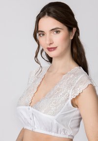 Weiße Bralette mit Spitzenbesatz am Ausschnitt und den Ärmeln, ausgestattet mit einem weichen Baumwollkörper und einer Knopfverschluss vorn. Glatte Textur.