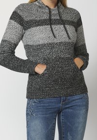 Grijze en zwarte gebreide pullover met hoge kraag, trekkoord en zijzakken. Heeft een gestructureerd patroon met horizontale strepen.