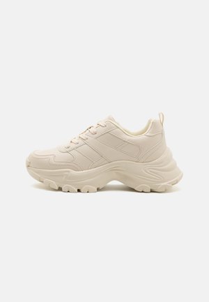 Beige chunky sneakers with textured faux leather, rounded toe, textured sole, and signature three-stripe design on the side.