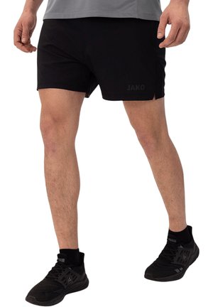 Man draagt zwarte sportshorts en zwarte sportschoenen, staat met iets gespreide benen op een witte achtergrond.