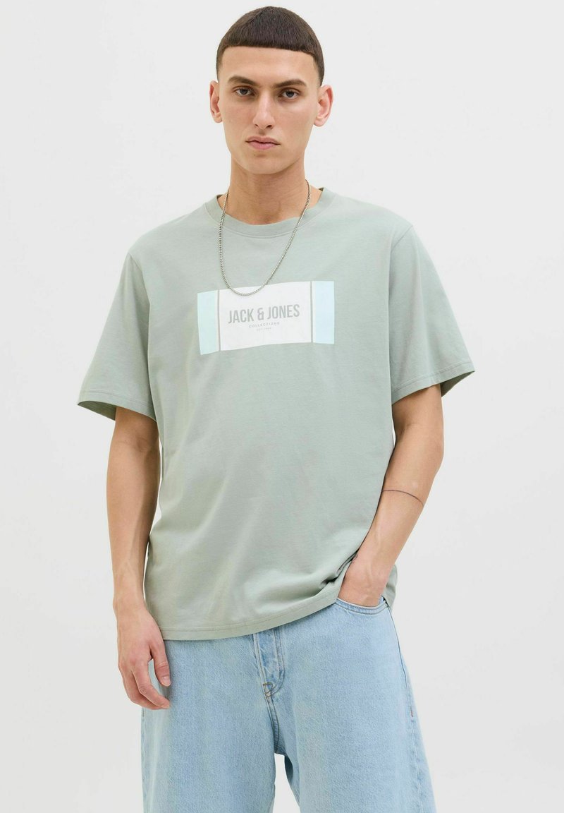 Kerge rohelise puuvillase lühikeste varrukate T-särk, millel on ristkülikukujuline valge ja helesinise graafika, kus keskel on "JACK & JONES".