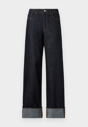 Donkerblauwe spijkerbroeken met brede pijpen, opgerolde manchetten in een lichtere denim, koperen stiksels, vijf zakken en een knoopsluiting.