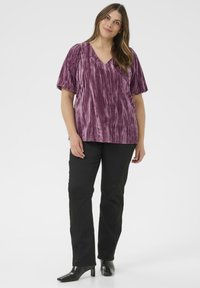 Blouse texturée violette avec un col en V et des manches courtes, associé à un pantalon droit noir et des bottines noires.