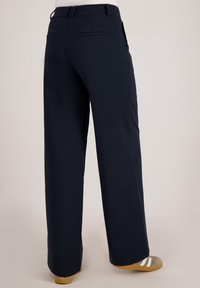 Marineblauwe wijde broek met een gladde textuur, voorzien van twee achterzakken en een tailleband. Accentueert met tan schoenen en subtiele plooien.