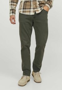 Pantalones de algodón verde oliva con corte recto, que presentan bolsillos laterales y traseros, combinados con zapatos de ante beige claro.